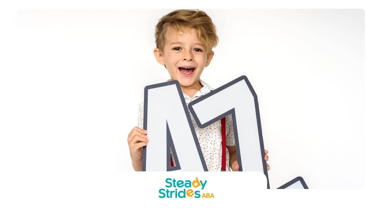 Young autistic boy holding large letters A and L, smiling during a playful early learning activity.