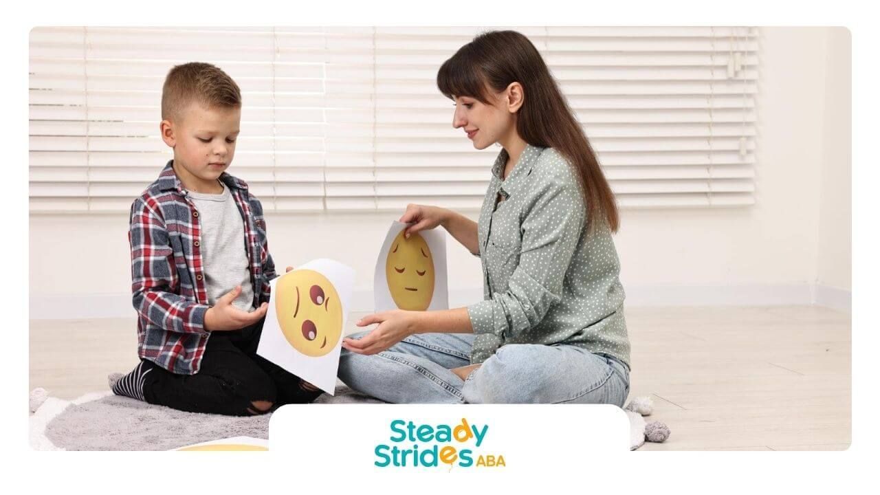 BCBA and autistic boy are holding emotion cards during ABA therapy.