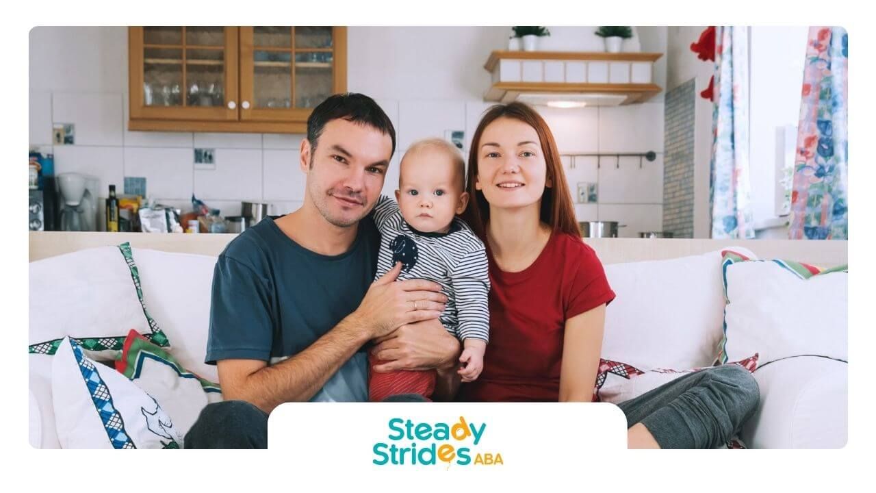 Smiling parents sitting on a couch with their autistic baby.