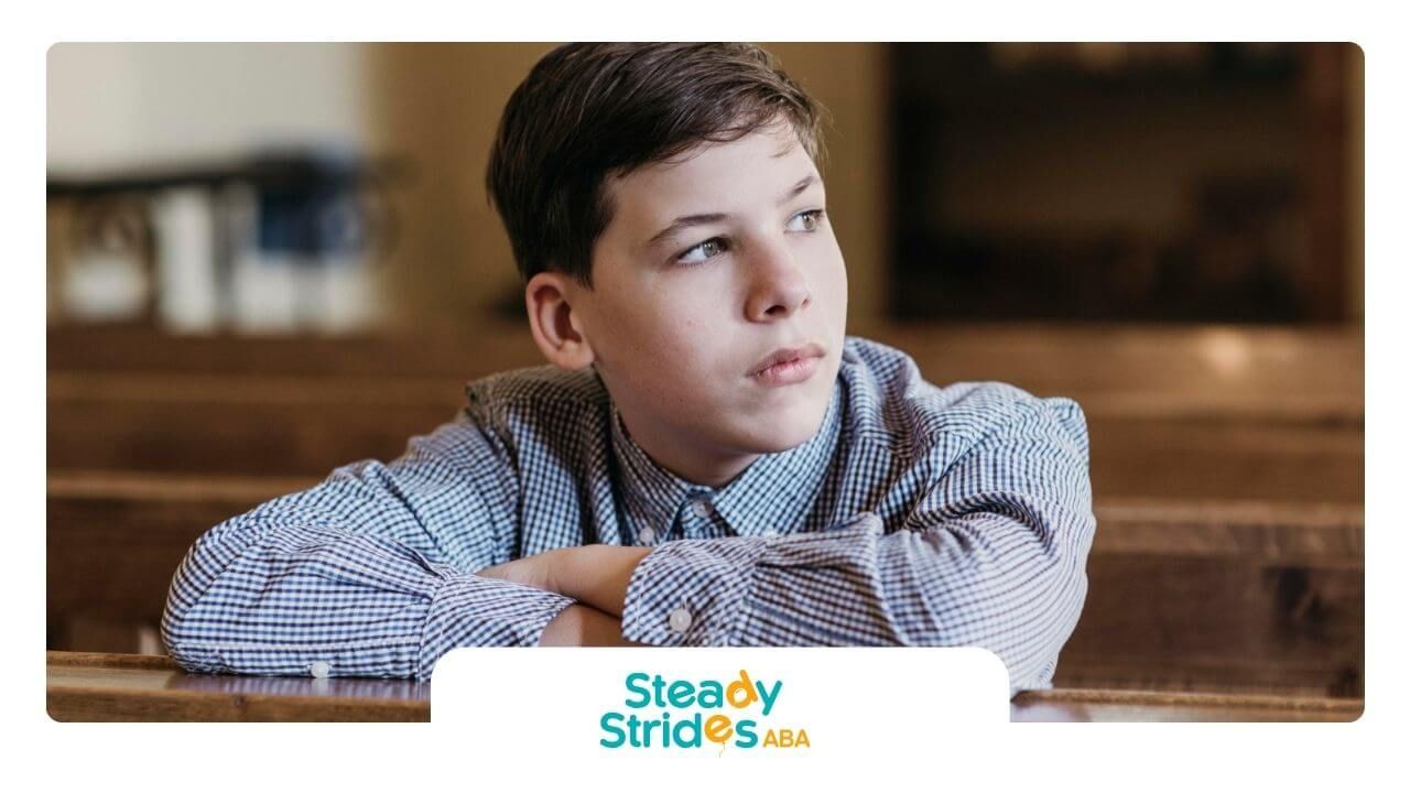 A boy with autism in checkered shirt sitting and looking to the side.