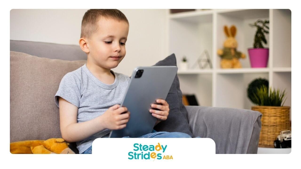 A young boy is sitting on a couch using a tablet computer.