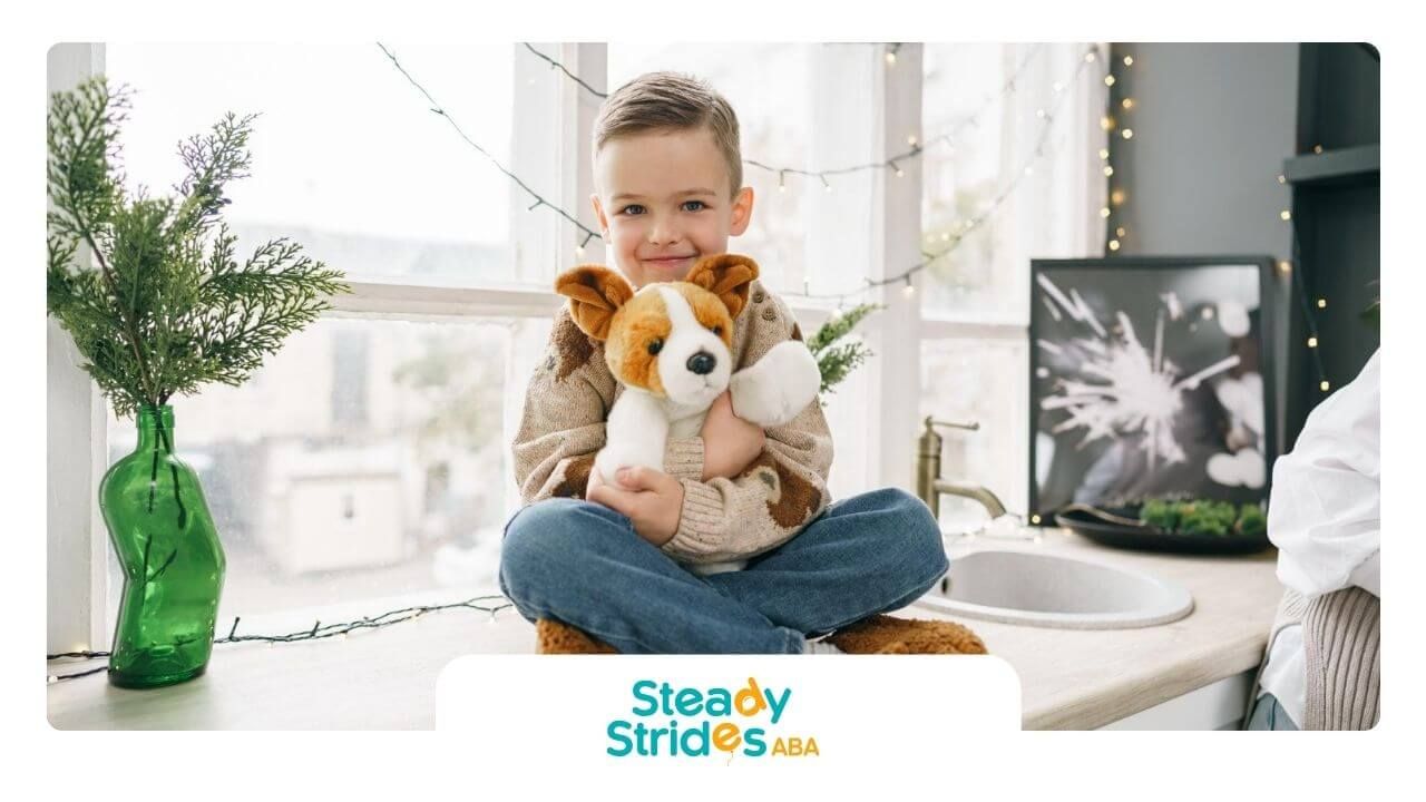 A young boy with autism is sitting on the floor holding a stuffed dog.