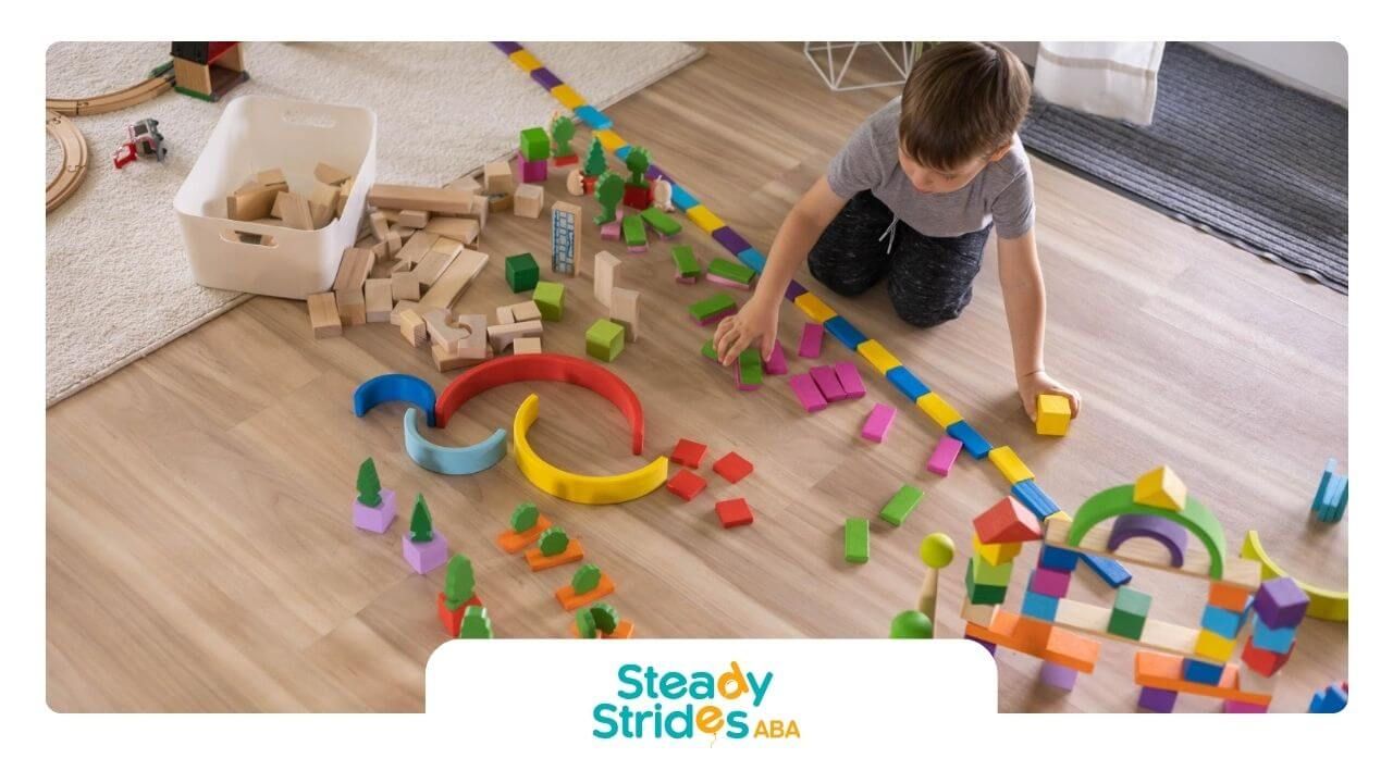 A child with autism lining up colorful wooden blocks and toys on the floor.