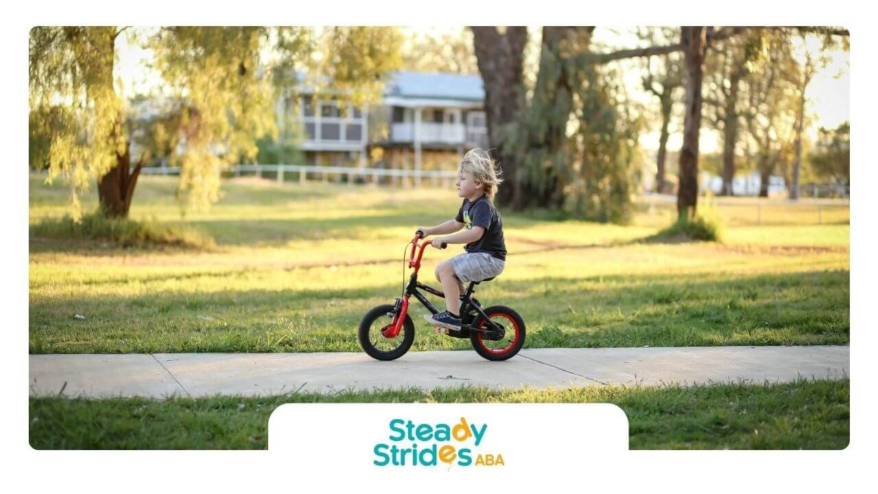 A young boy is riding a bike down a sidewalk in a park after an ABA therapy session.