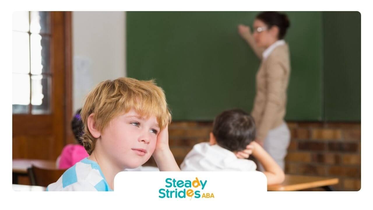 A bored student with autism staring into the distance while a teacher writes on the chalkboard.