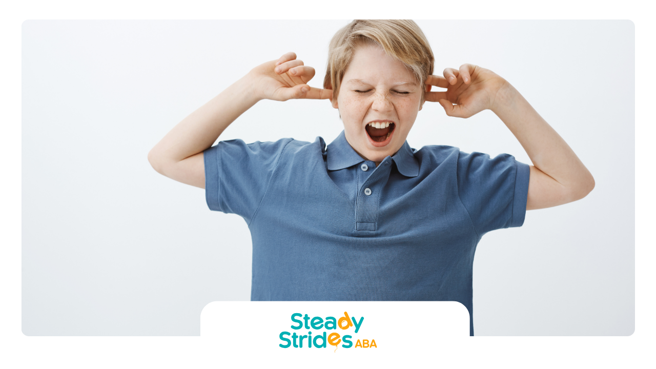 A boy in a blue shirt is covering his ears with his hands