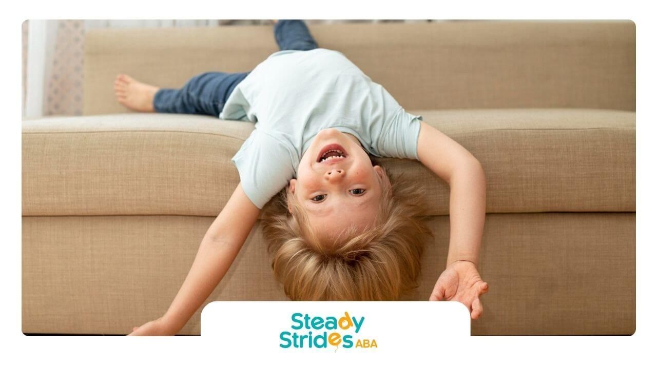 A young boy with autism is doing a handstand upside down on a couch.