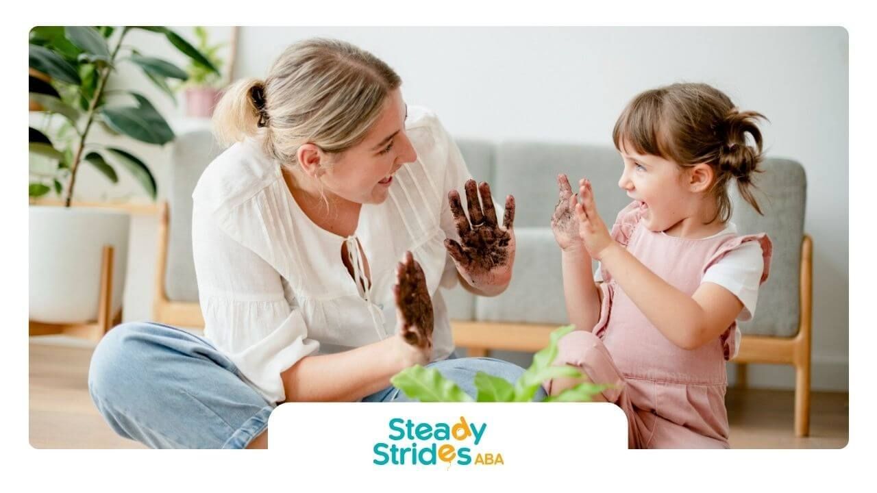 An ABA therapist and a little girl are sitting on the floor playing with pine cones in ABA therapy.