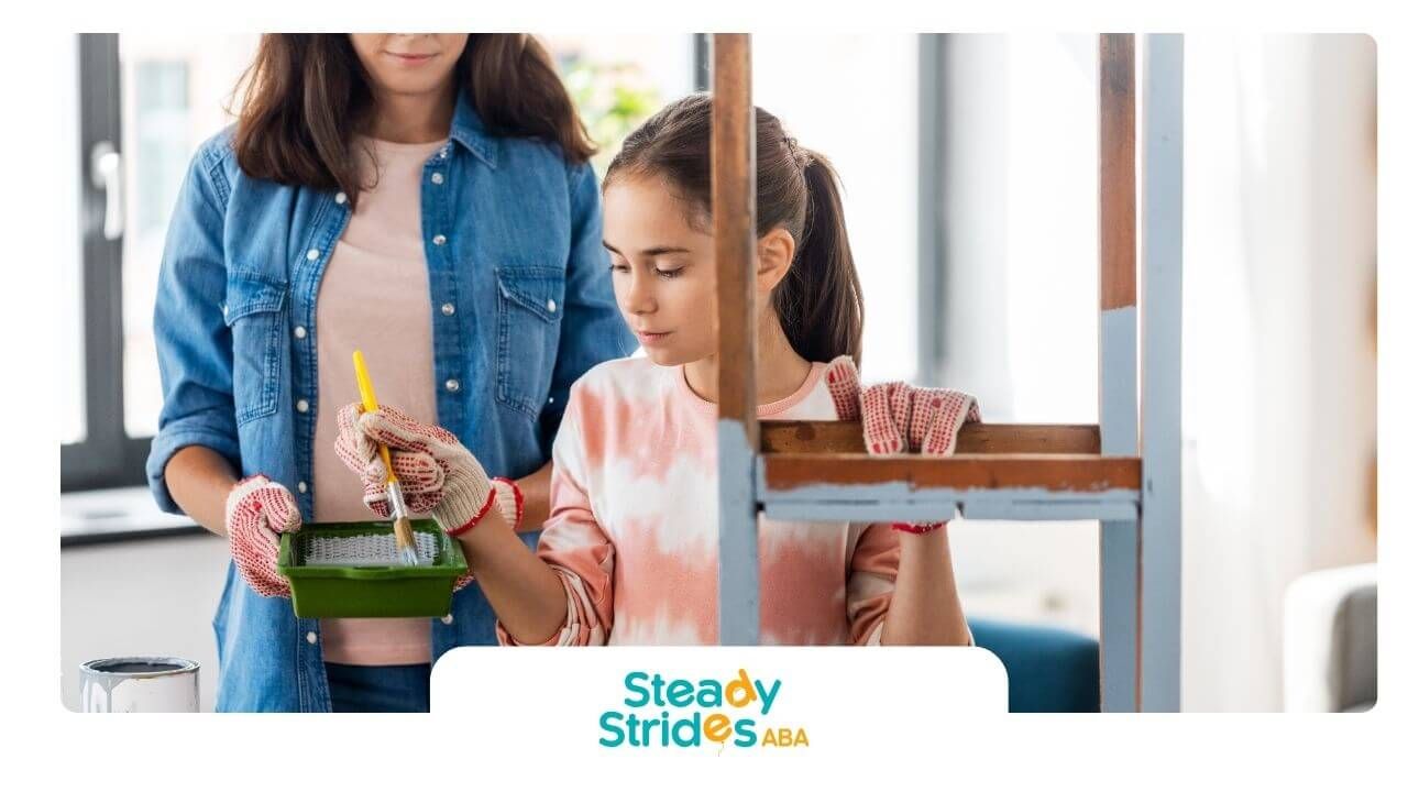Therapist and autistic girl wearing gloves painting a wooden chair together during a DIY project.