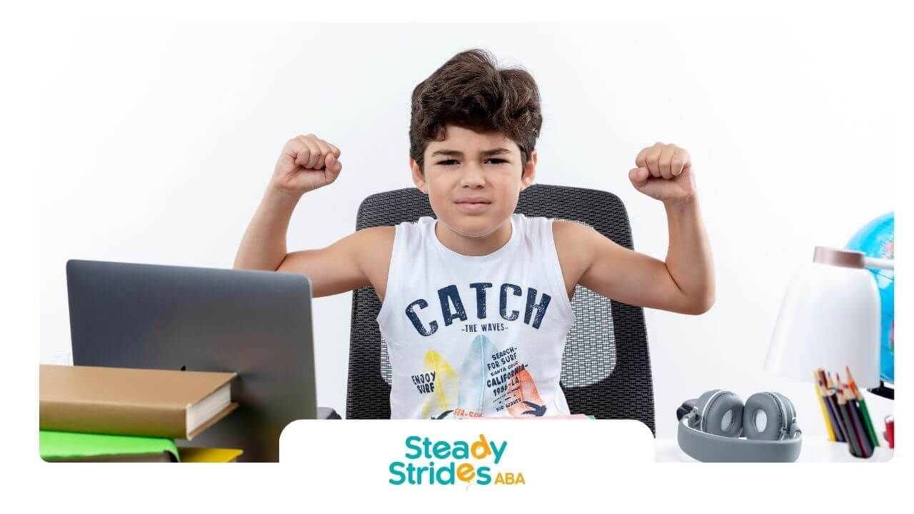 Autistic boy sitting at a desk flexing his arms proudly, showing confidence while studying.