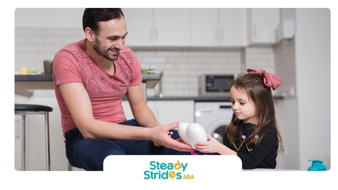 Therapist & and autistic girl sitting at a table painting a craft together & promoting creativity.