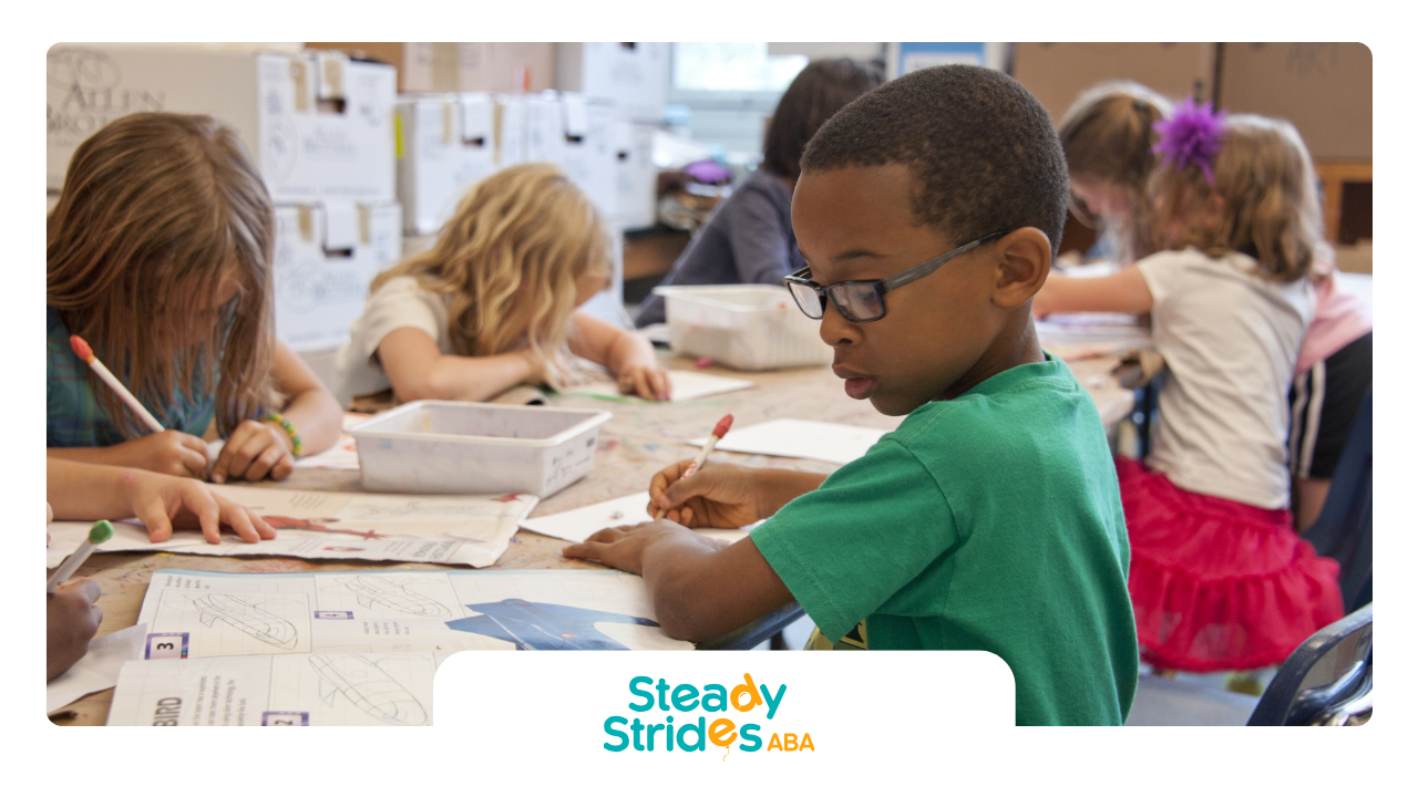 Children drawing at a table. One child wearing glasses and a green shirt, others have blond hair and are wearing white shirts.