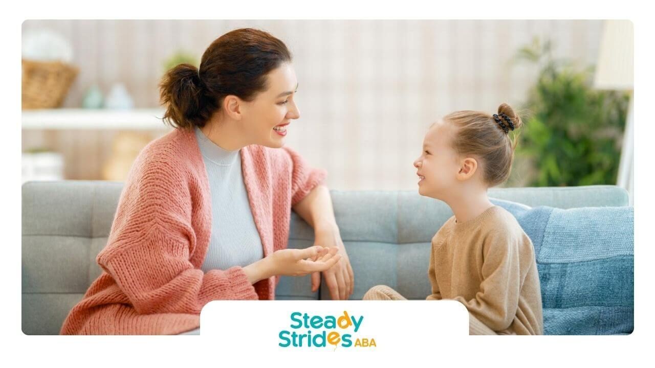 Smiling BCBA talking with her autistic girl while sitting together on a couch in ABA therapy.