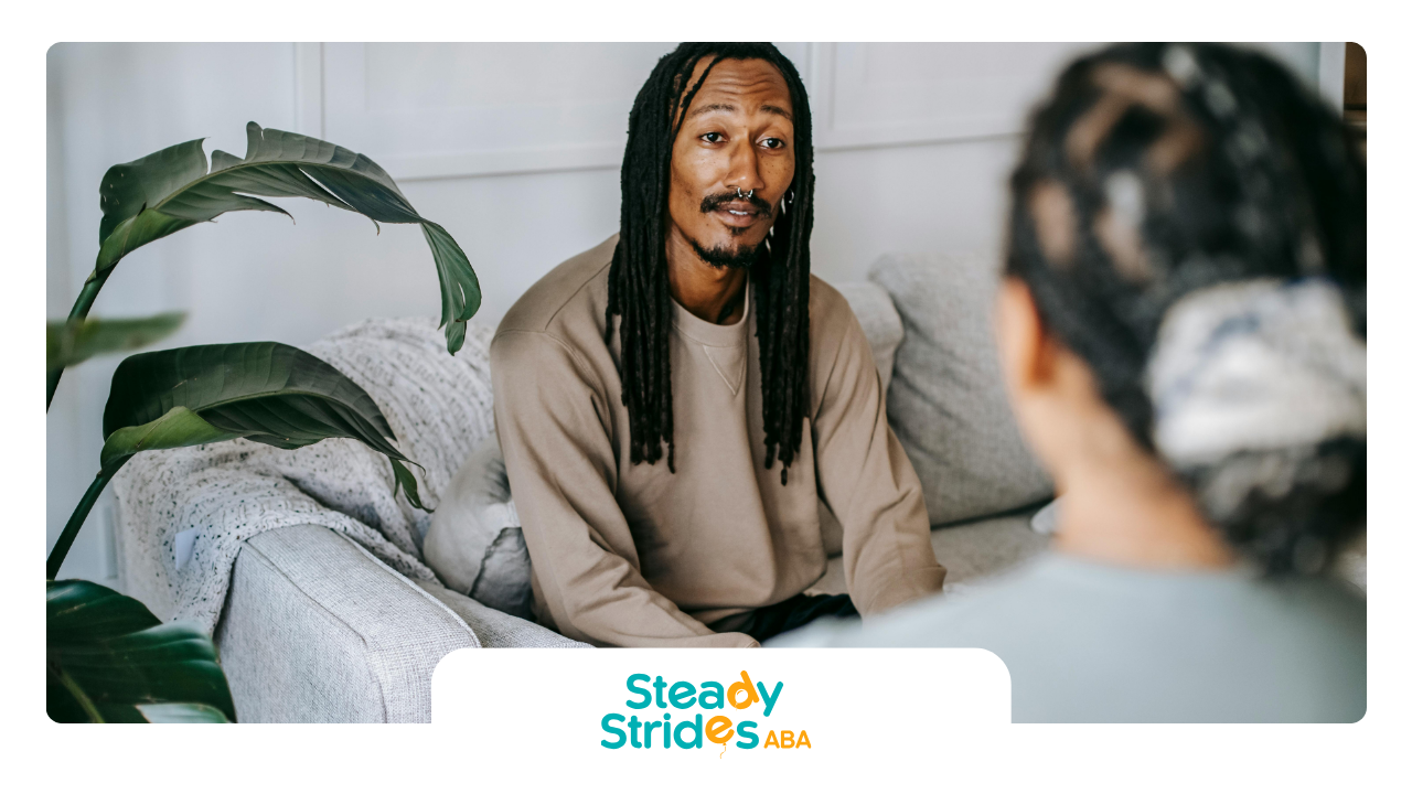 A man with dreadlocks is sitting on a couch talking to a woman.