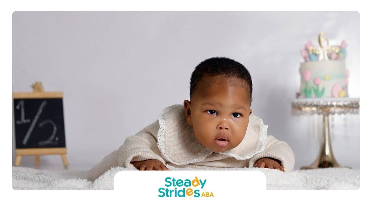 Autistic baby in lace outfit lies on fluffy surface beside cake and chalkboard after ABA Therapy