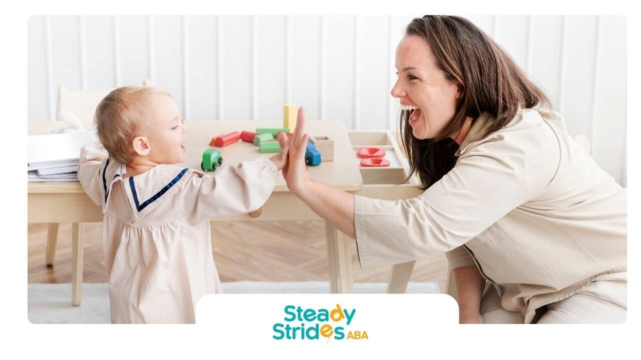 Therapist high-fives autistic toddler at play table with colorful toy blocks at home after therapy.