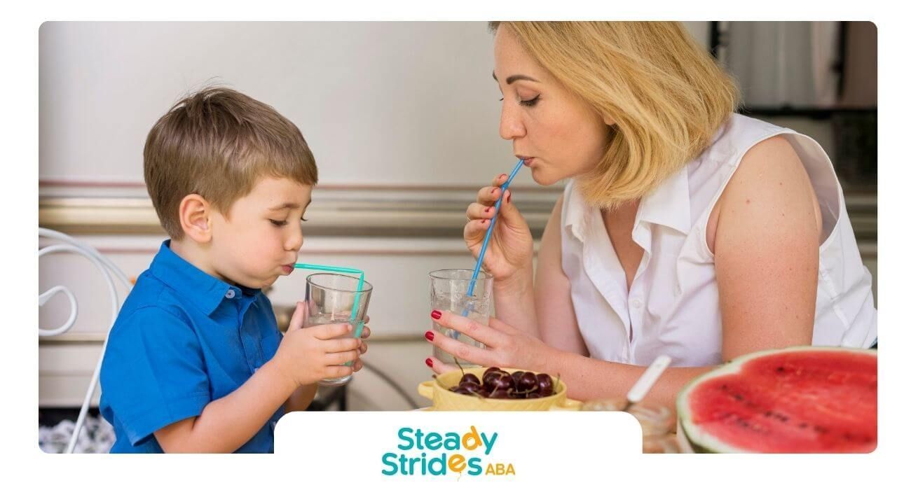 Therapist and autistic boy drink lemonade with straws at kitchen table with fruit after therapy.
