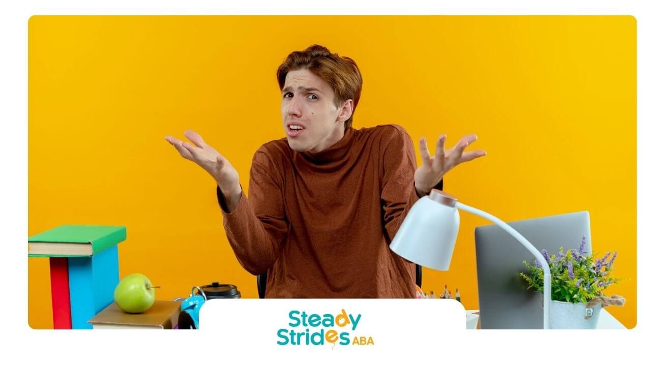 Confused therapist sitting at a desk with books and supplies, shrugging while studying indoor