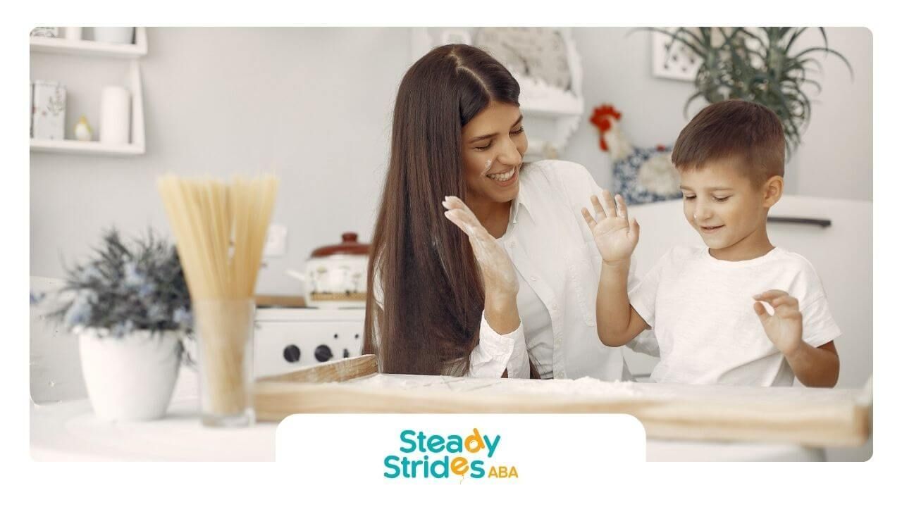A BCBA and young boy with autism smiling while baking together in the kitchen.