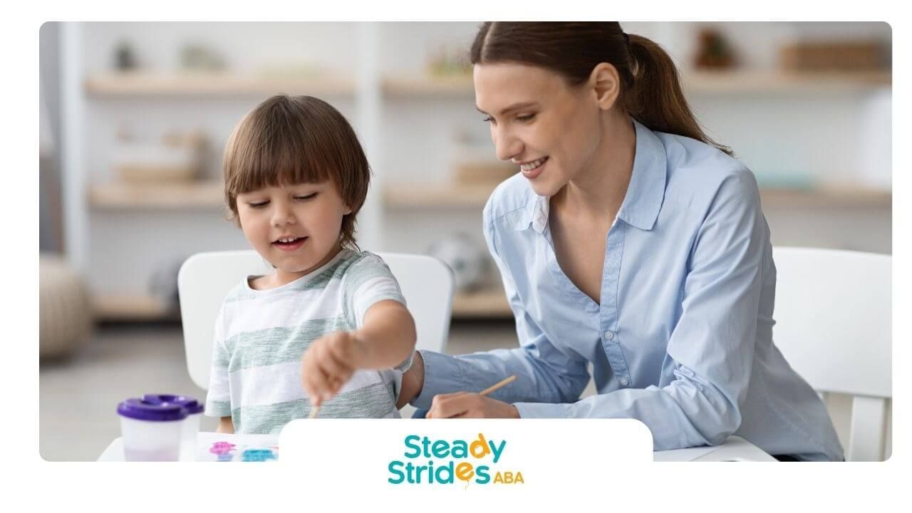 Therapist smiling as autistic child paints with bright colors during creative learning activity.