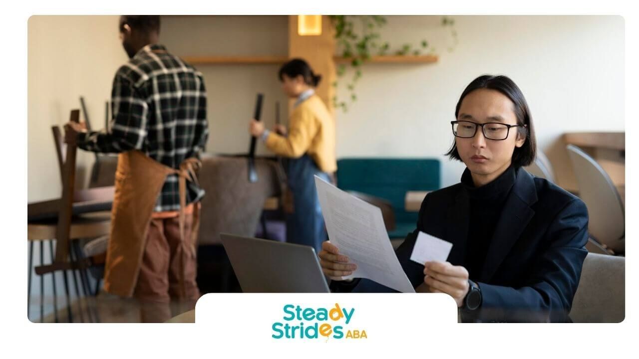 ABA therapist reviewing paperwork at a café table while staff prepare the space in the background