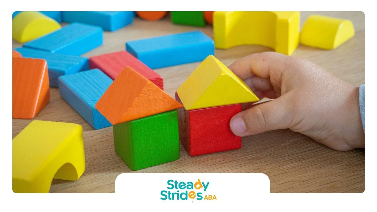 Autistic child’s hand arranging wooden blocks into houses during school-based ABA therapy in Texas.