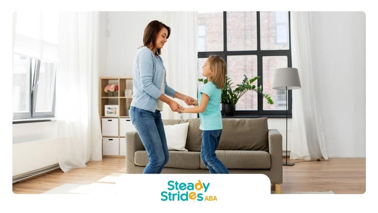 BCBA and autistic girl smiling and dancing together in a bright living room during ABA therapy.