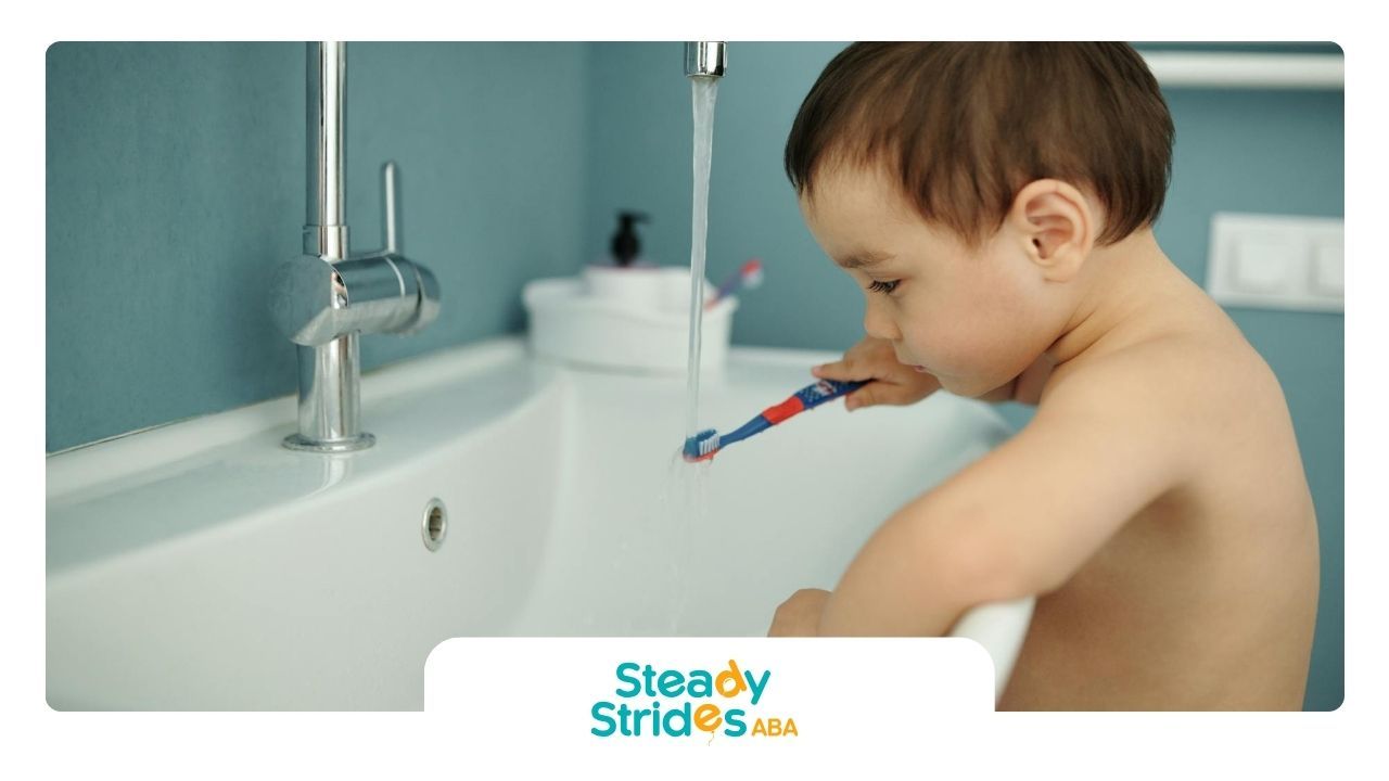 An autistic toddler rinsing a toothbrush under running tap water in a bathroom sink at home in TX.