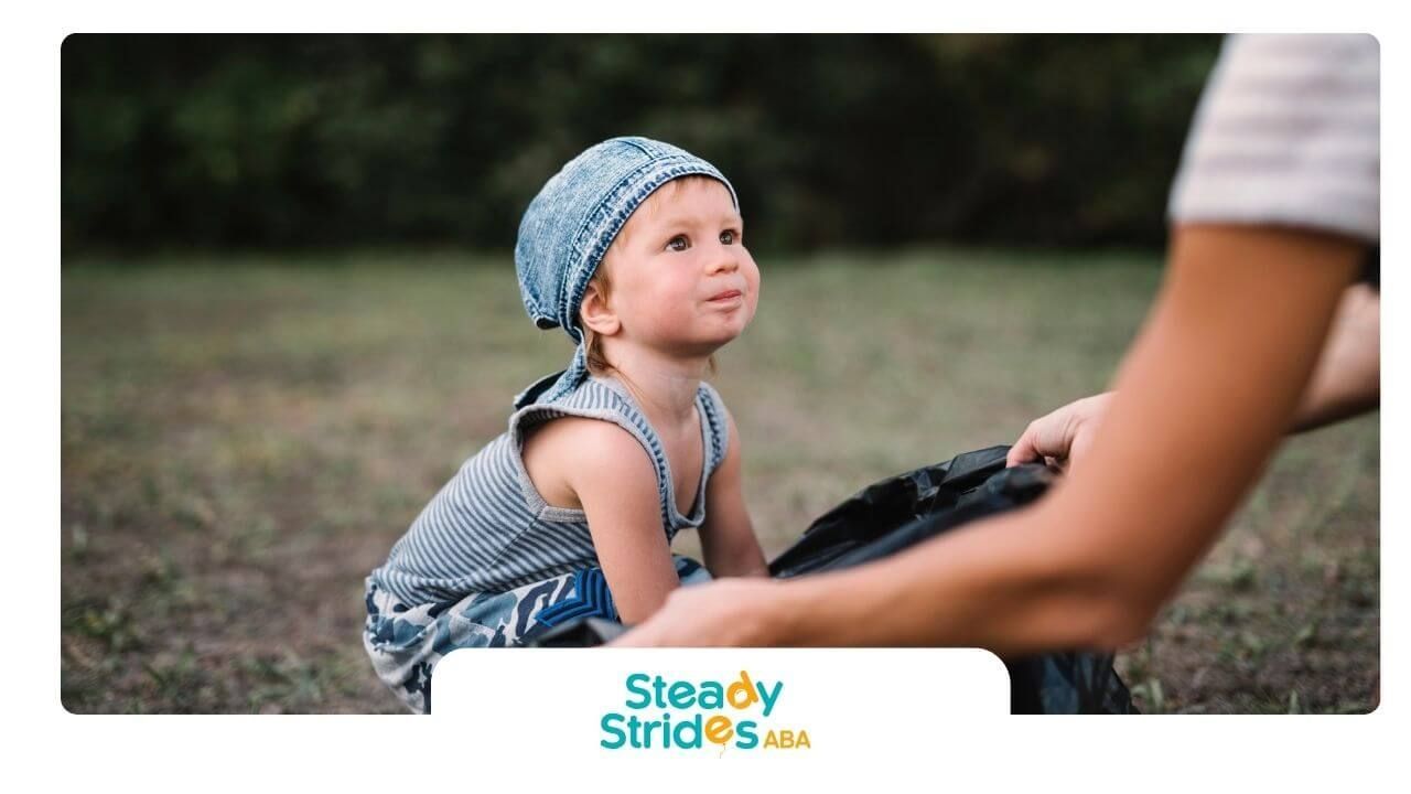 Autistic kid sitting on the ground outdoors, looking up at an adult during a caring interaction.