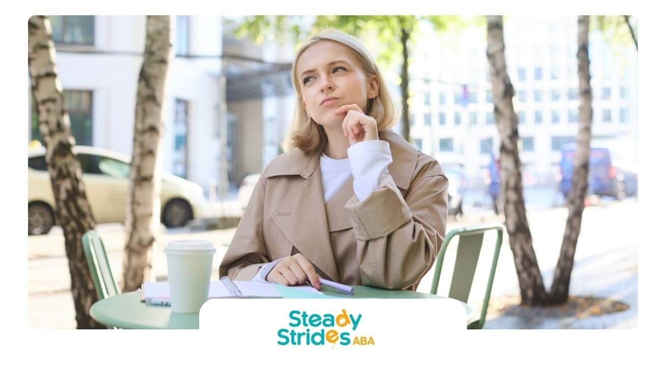 Smiling ABA in cap and gown holding coffee and a speech bubble sign, celebrating academic success.