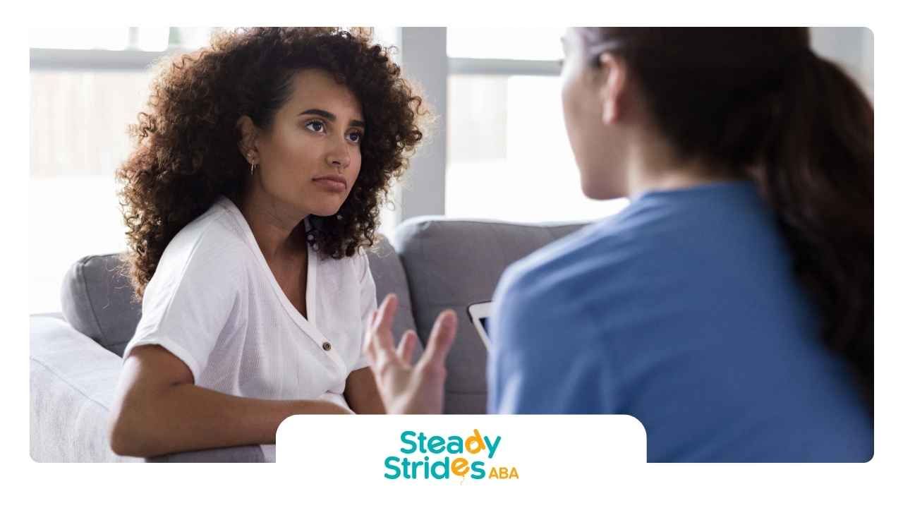 Two women are sitting on a couch talking to each other.