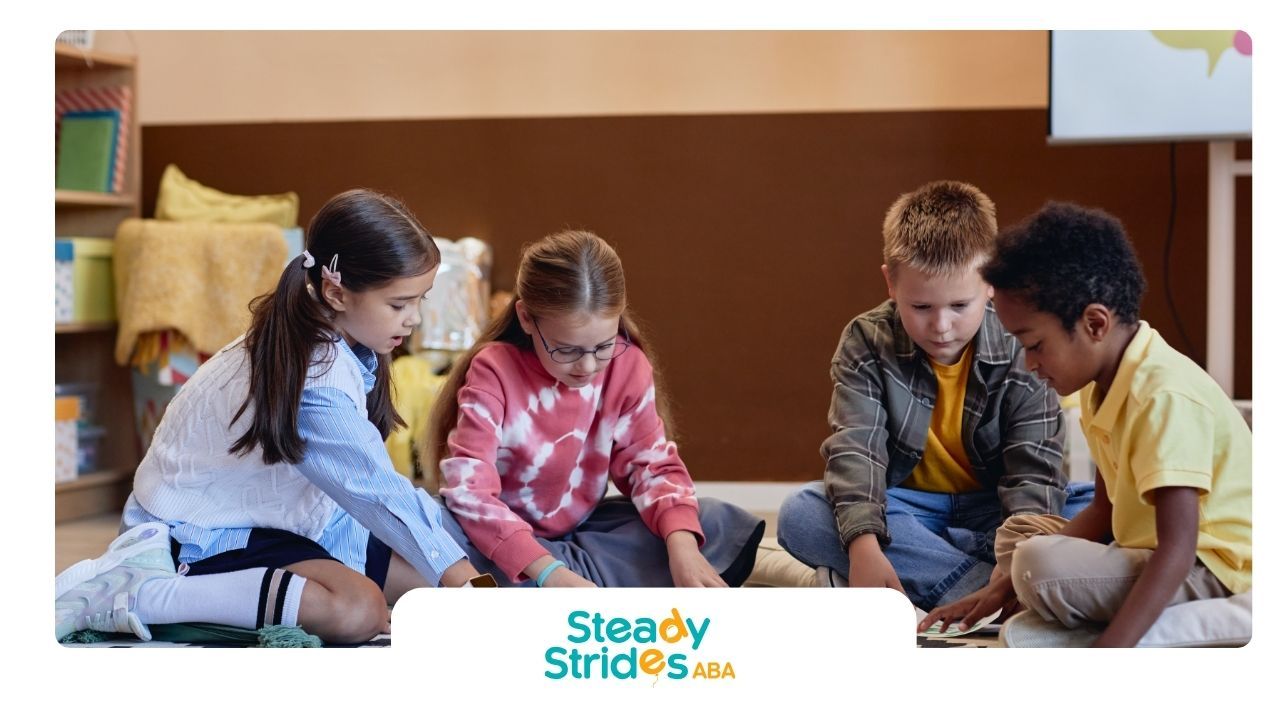 Four children sitting on floor, looking at something on rug.  Classroom setting, brown wall, light background.