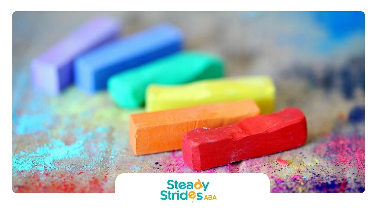 Chalk sticks on surface with scattered powder in bright hues, symbolizing autism spectrum awareness.