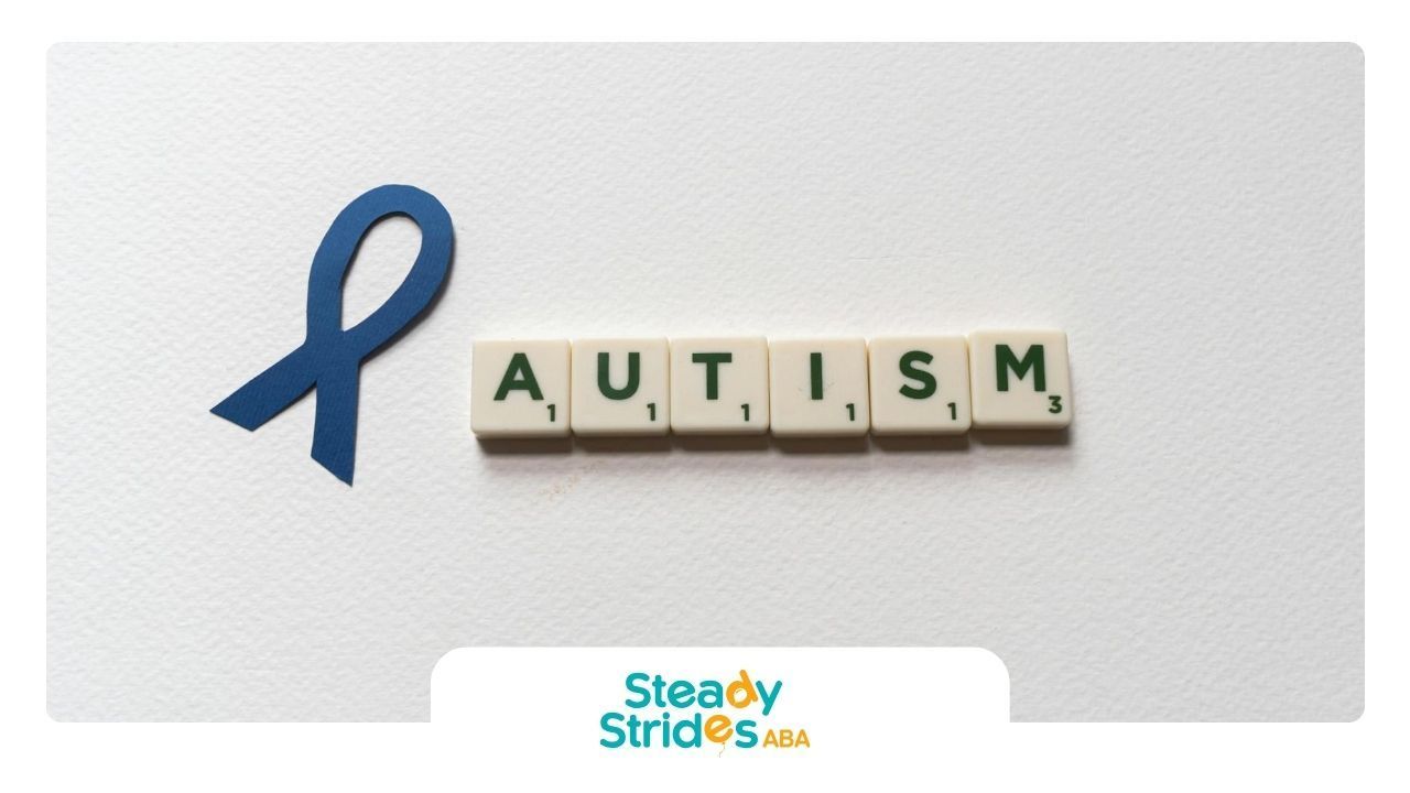 Blue ribbon with letter tiles spelling “AUTISM” on white background, symbolizing autism awareness.
