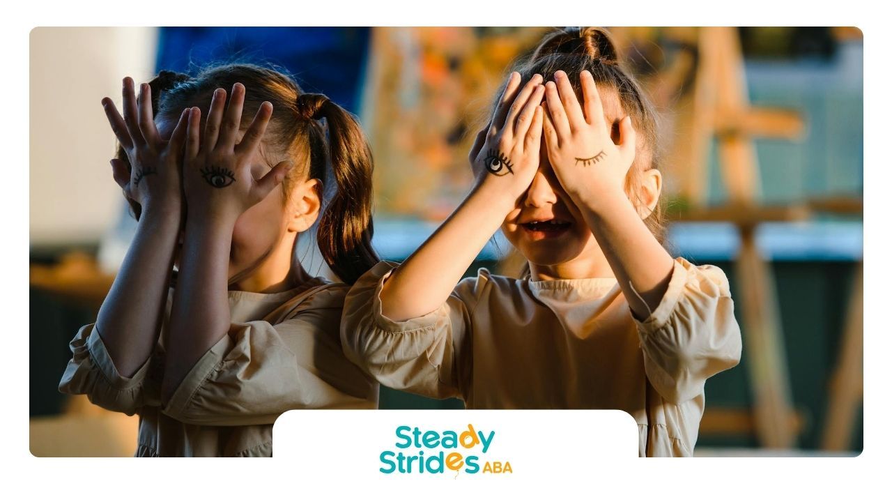 Two autistic girls playfully covering their eyes with hands that have drawn eyes on them in Texas.