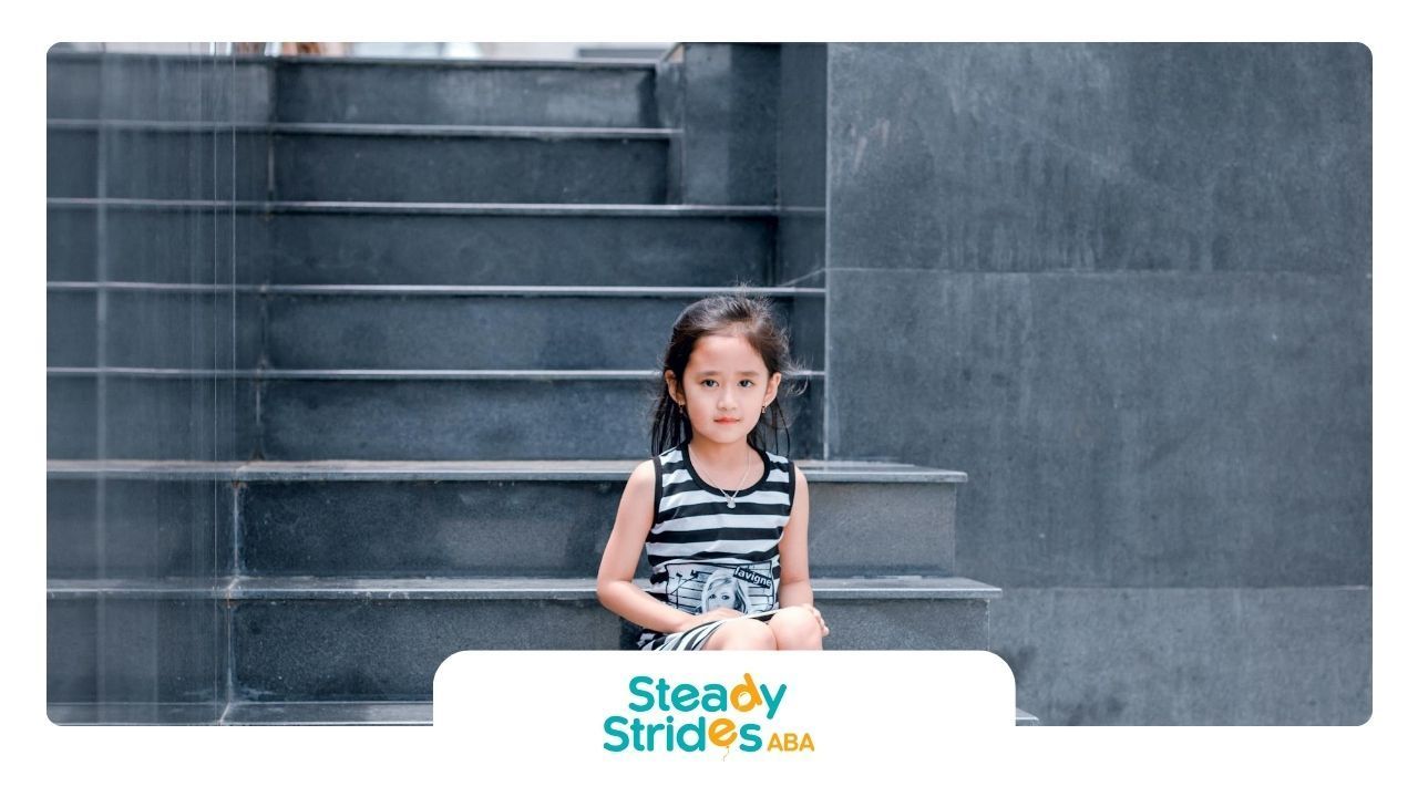 An autistic little girl sitting alone during an ABA therapy session on outdoor steps in New Mexico.