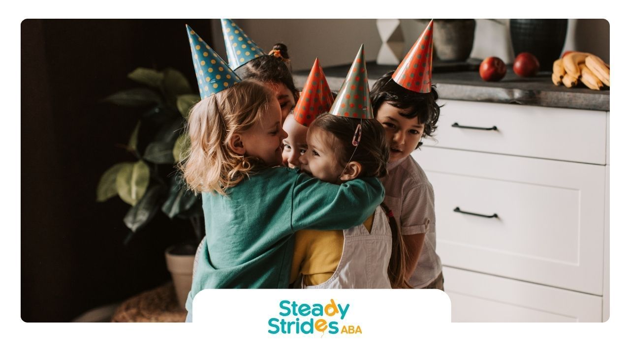 Four children in party hats hug, near white cabinets.