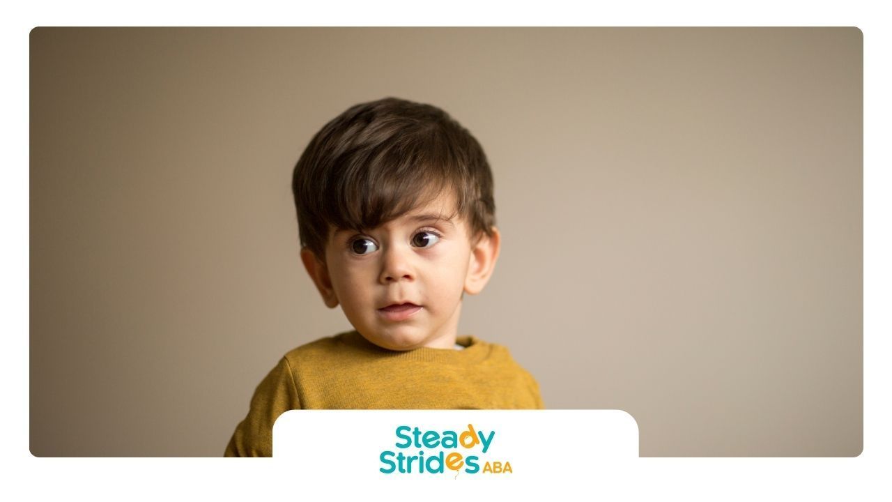 A little boy in a yellow shirt is looking at the camera.