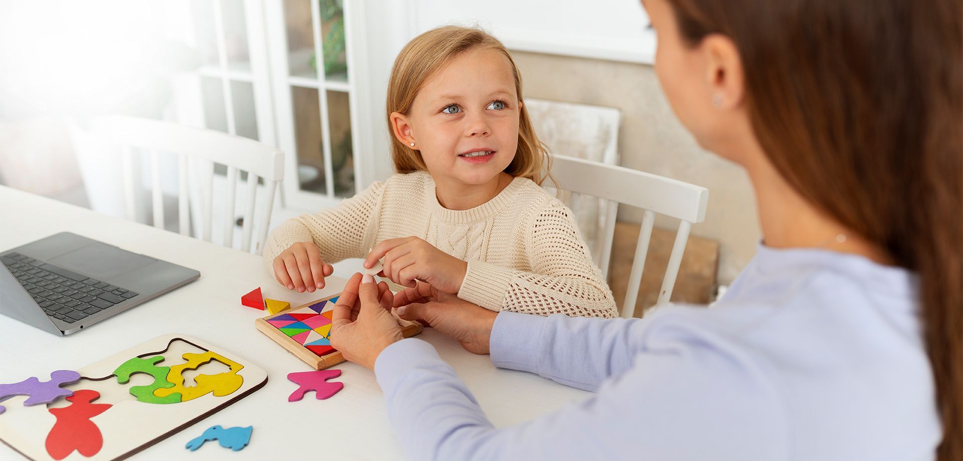 A woman and a little girl sitting at a table playing with puzzles.