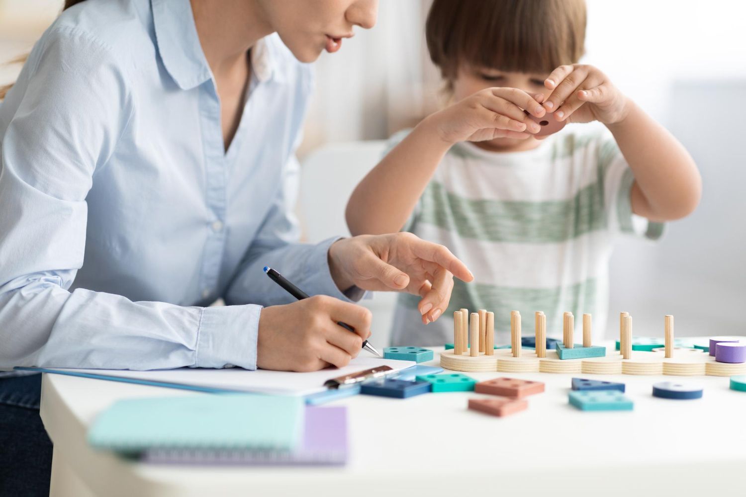 A woman and a child are playing with wooden blocks at a table.