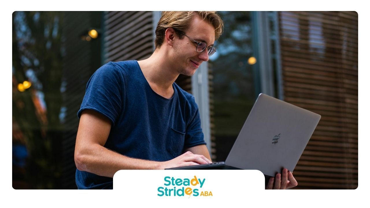 A young man wearing glasses and a blue t-shirt finding RBT jobs near him in TX on his laptop.