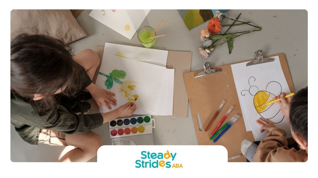 Two children are sitting at a table drawing a bee on a piece of paper.