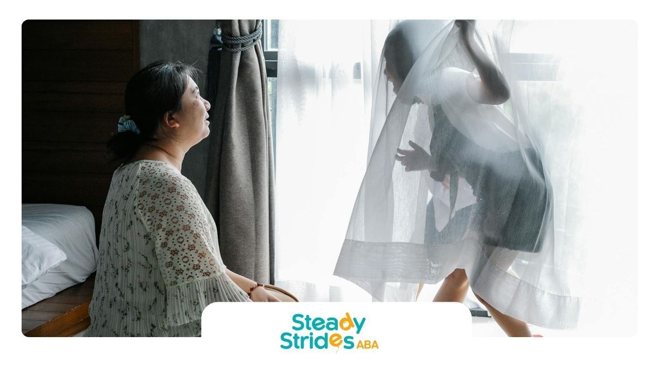 Child playing peekaboo behind curtain while an RBT watches with a smile during ABA therapy in TX.