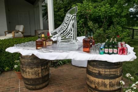 Outdoor rustic drink table with white cloth, barrels, lanterns, and bottled beverages on a porch