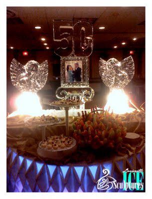 50th birthday dessert table with large gold “50,” sparkling angel wings, and lit candles