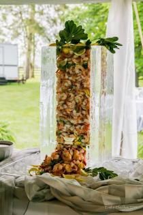 Tall glass vase of layered food salad centerpiece on a table at an outdoor event