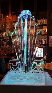 Glowing blue ice sculpture centered in a dim bar, with bottles on shelves behind it.