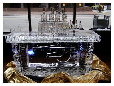 Clear ice sculpture with a carved car, lit blue, displayed outdoors on a golden cloth.
