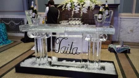Elegant glass fountain centerpiece with white flowers and the name “Gaila” on a black-and-white display table.