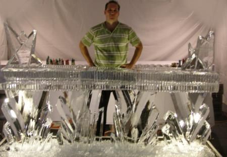Man standing behind a silver, reflective sculpture-like structure in a draped indoor setting